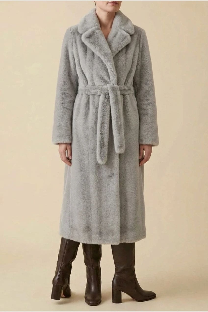 Woman wearing a long belted faux fur coat with notch lapels, tie waist and full-length sleeves, holding a suede tote and wearing knee-high boots._14