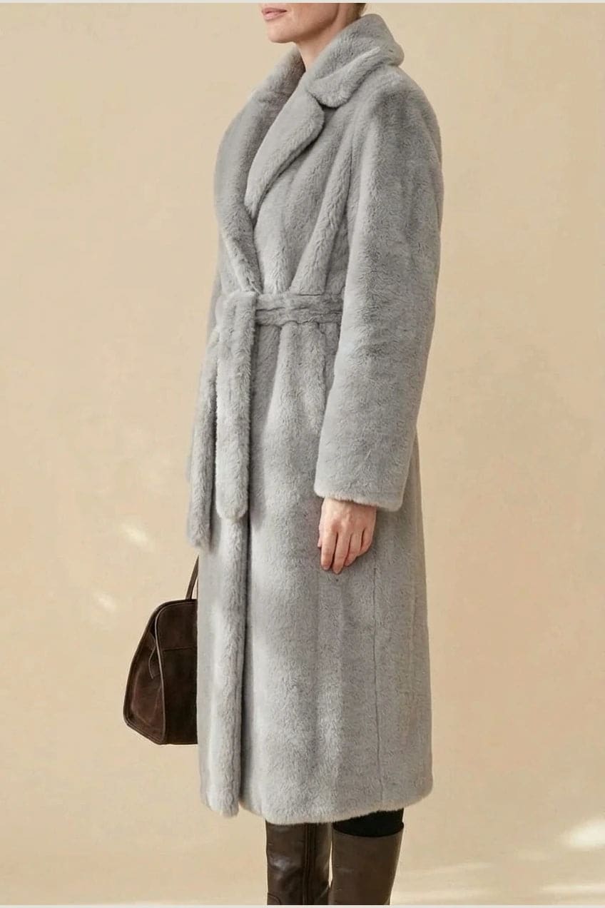 Woman wearing a long belted faux fur coat with notch lapels, tie waist and full-length sleeves, holding a suede tote and wearing knee-high boots._16