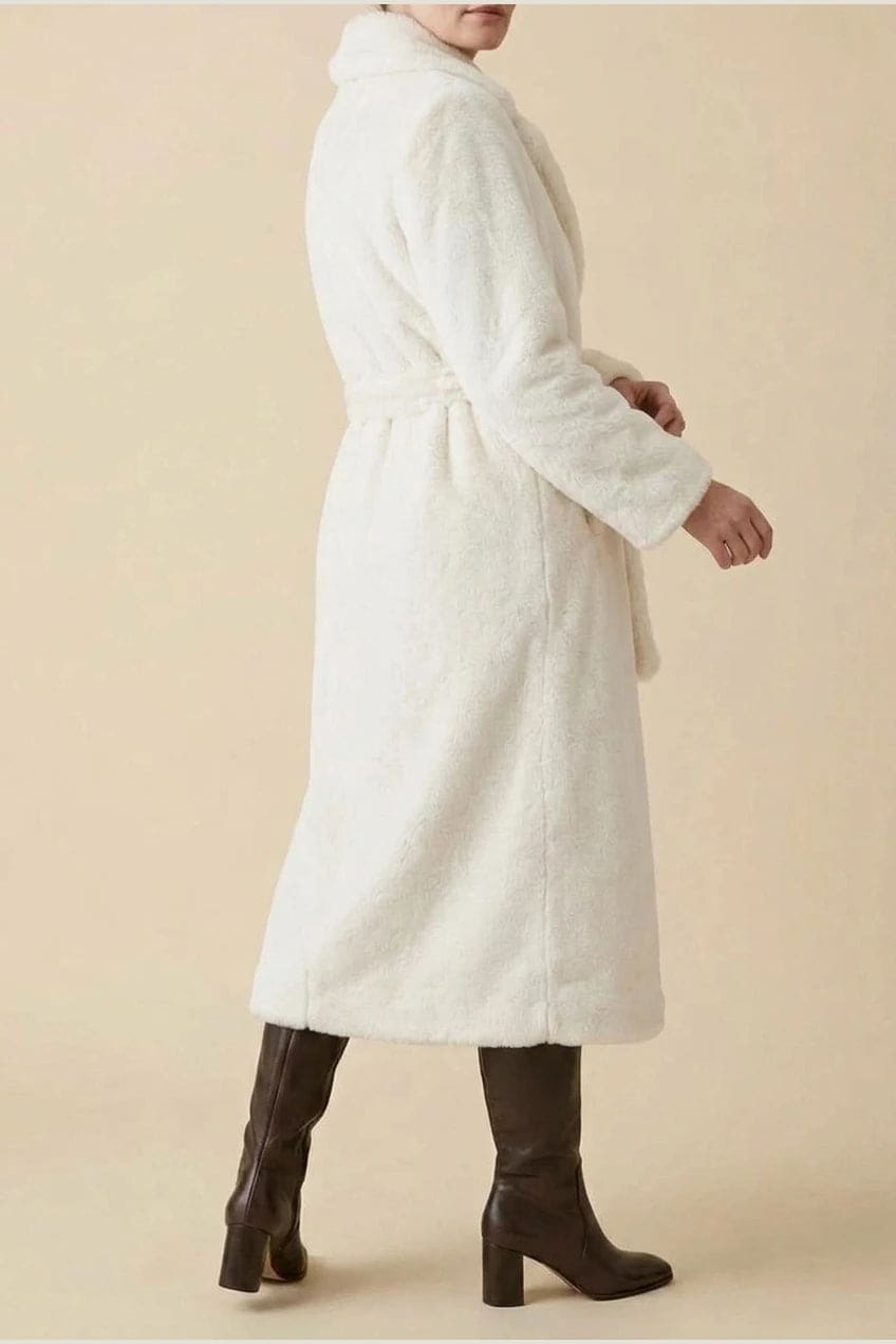 Woman wearing a long belted faux fur coat with notch lapels, tie waist and full-length sleeves, holding a suede tote and wearing knee-high boots._2