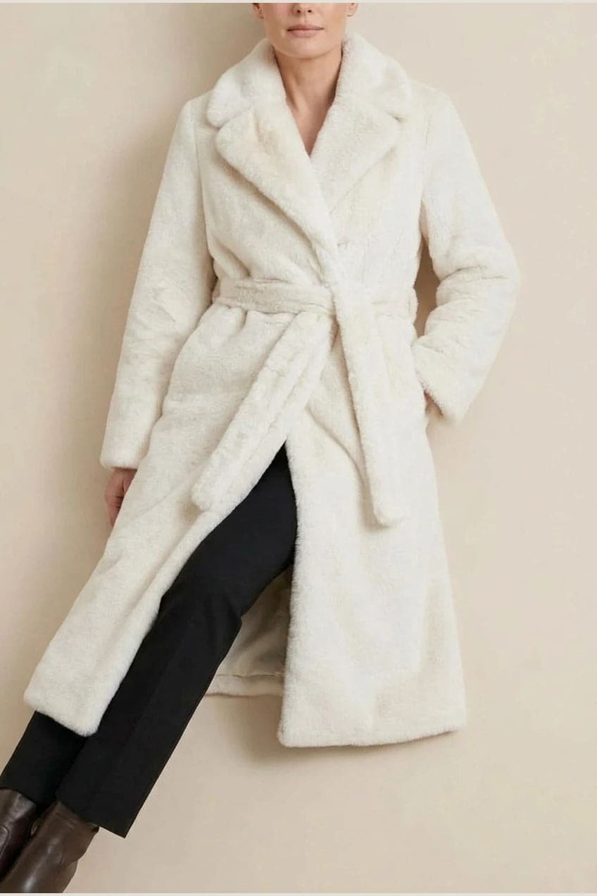 Woman wearing a long belted faux fur coat with notch lapels, tie waist and full-length sleeves, holding a suede tote and wearing knee-high boots._3