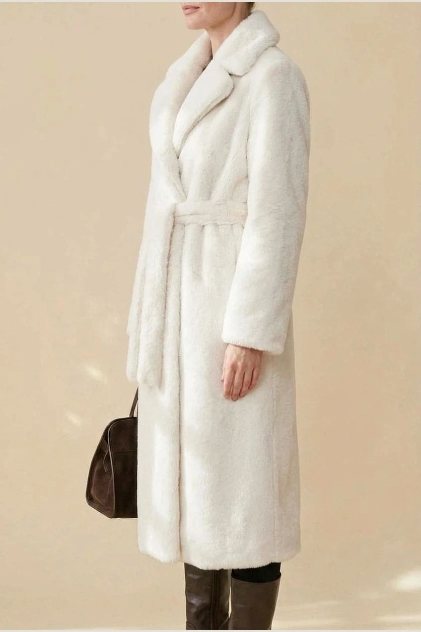 Woman wearing a long belted faux fur coat with notch lapels, tie waist and full-length sleeves, holding a suede tote and wearing knee-high boots._4