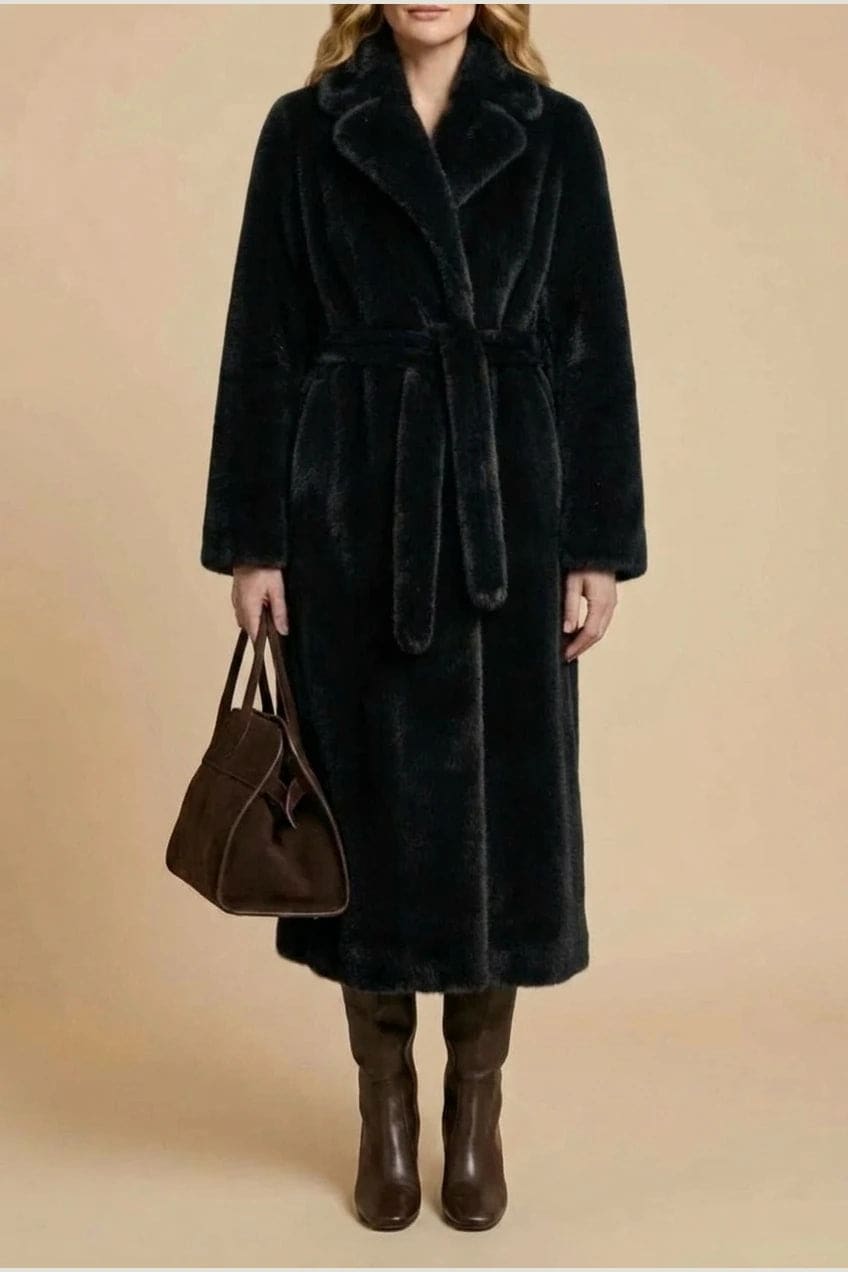 Woman wearing a long belted faux fur coat with notch lapels, tie waist and full-length sleeves, holding a suede tote and wearing knee-high boots._7