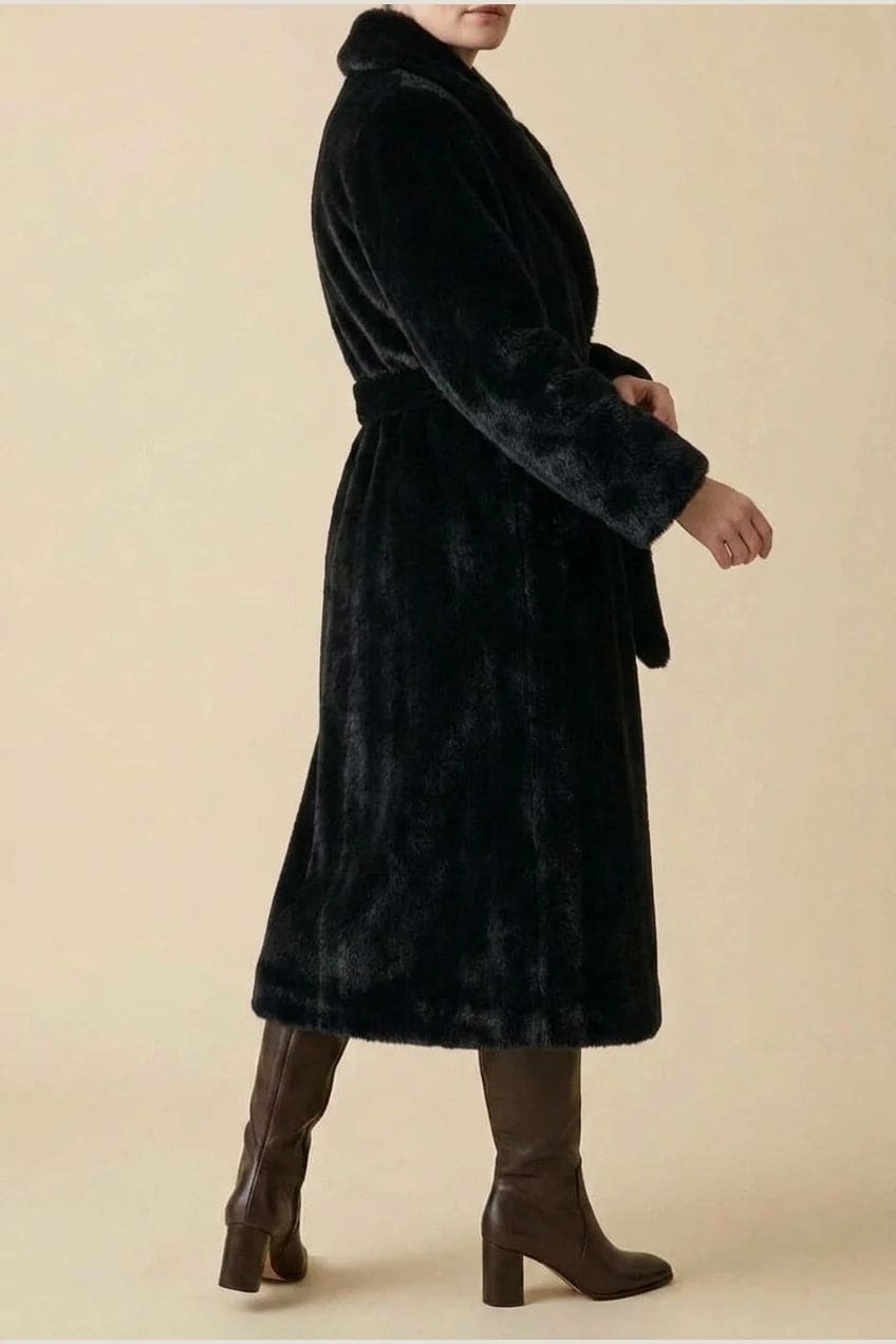 Woman wearing a long belted faux fur coat with notch lapels, tie waist and full-length sleeves, holding a suede tote and wearing knee-high boots._8