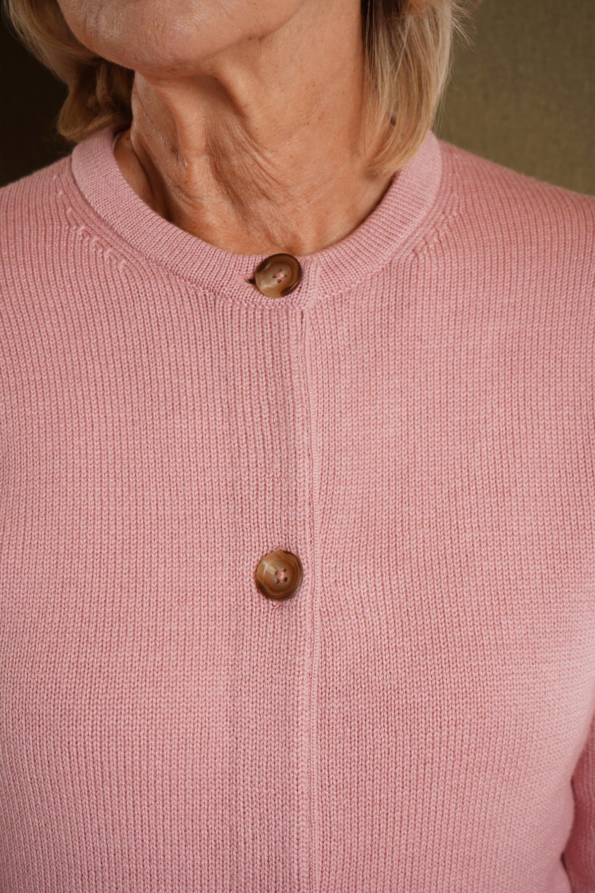 Woman seated wearing a long sleeve knit cardigan with round neck, full button front and ribbed cuffs and hem, with jeans._7
