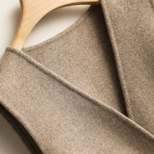 A sleeveless wrap vest with a V neckline, defined waist seam, and single front button displayed on a wooden hanger._5