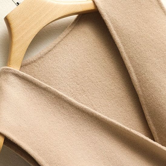 A sleeveless wrap vest with a V neckline, defined waist seam, and single front button displayed on a wooden hanger._7
