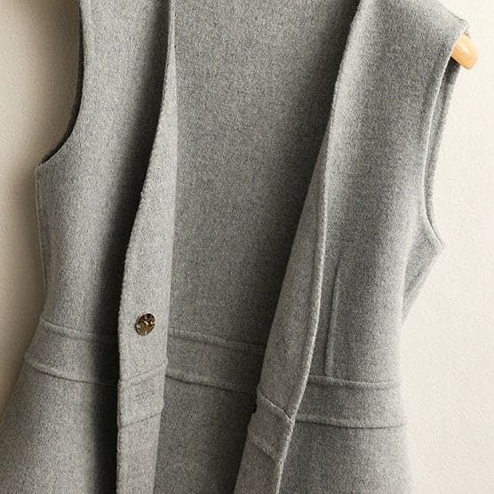 A sleeveless wrap vest with a V neckline, defined waist seam, and single front button displayed on a wooden hanger._8