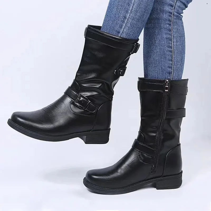 Black mid-calf biker boots with low heels, buckle straps, side zippers, and rounded toes shown with jeans.