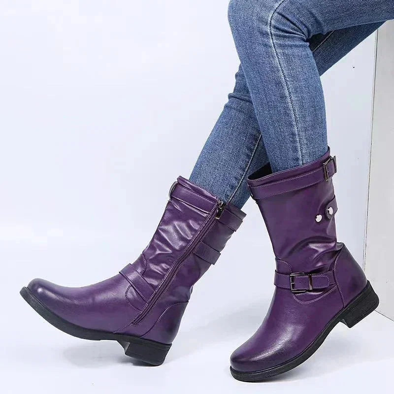 Purple mid-calf biker boots with low heels, multiple buckle straps, and side zippers paired with blue jeans.