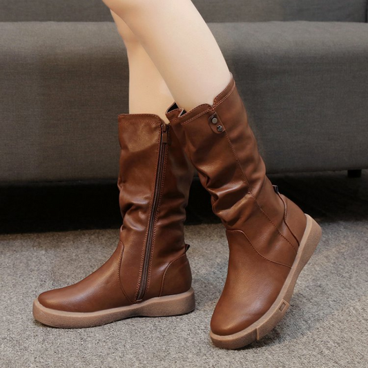 Brown mid-calf boots shown worn with one boot crossed in front, featuring softly gathered shafts, side zips and low wedge heels.