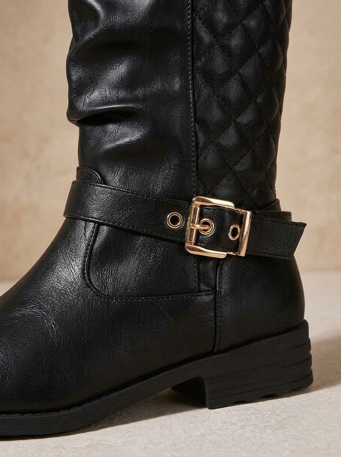 Detailed view of a black boot's ankle buckle, gathered shaft, stitching, and low block heel.