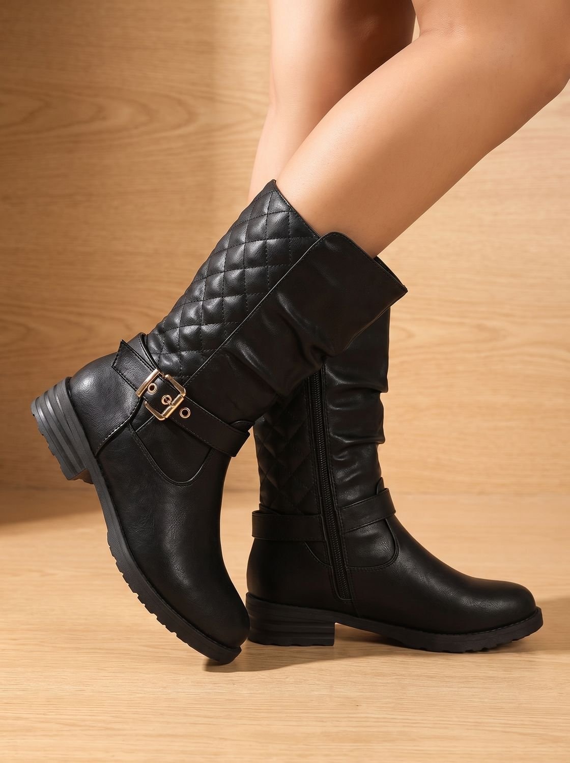 Black slouch boots shown from the side, highlighting the quilted upper shaft, ankle buckle straps, and low block heels.