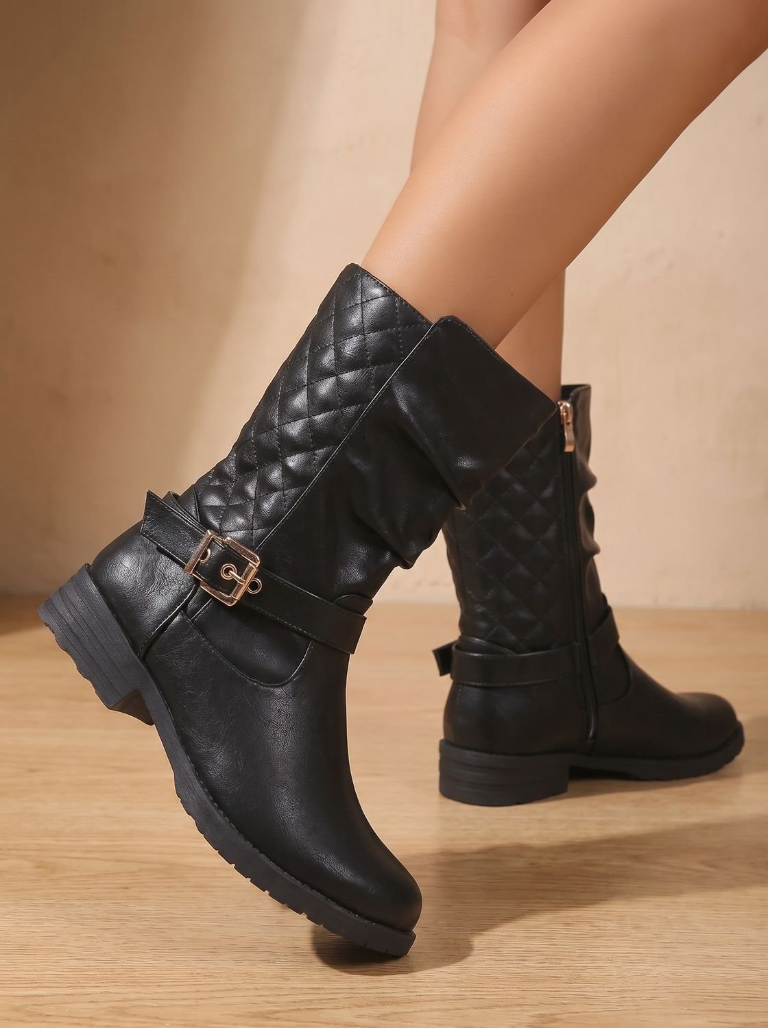 Close side view of a black boot with a quilted shaft, gathered front, gold-tone buckle, and textured sole edge.
