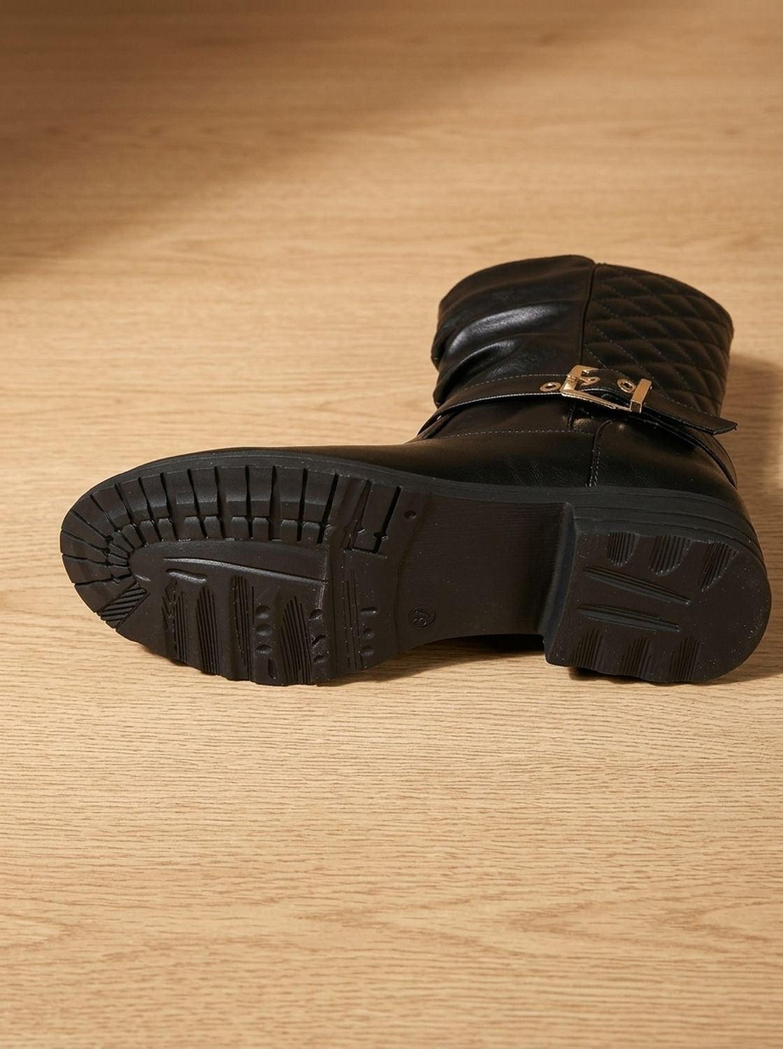 Bottom view of black boots displaying their deeply grooved lug soles and low stacked heels.