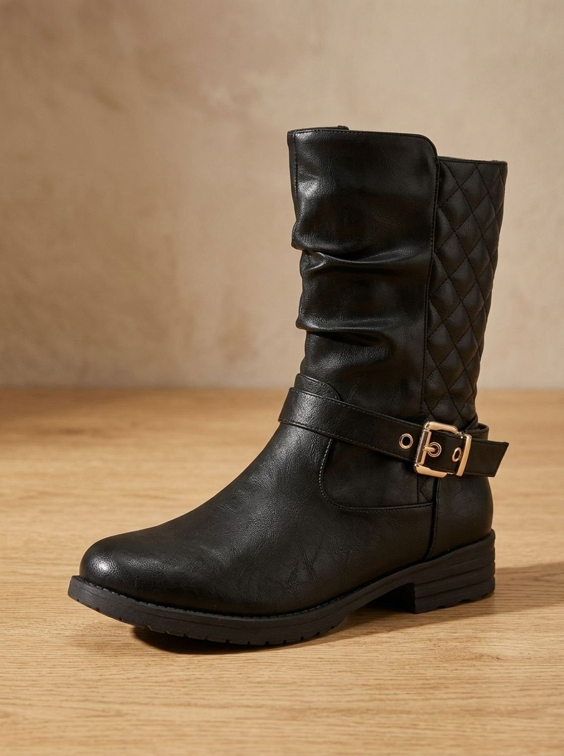 Single black mid-calf slouch boot standing upright, featuring a rounded toe, ankle buckle, quilted shaft, and low heel.