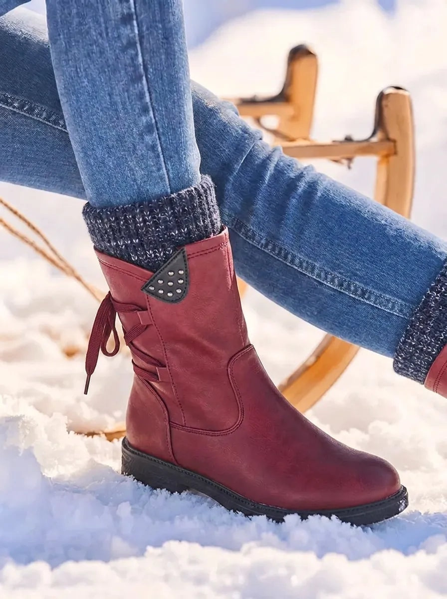Burgundy red mid-calf winter boot in snow, featuring a matching knitted cuff, side zip and decorative studded side detail.
