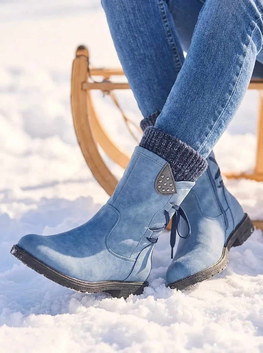 Light blue mid-calf boots angled in the snow, highlighting the rounded toes, side lacing details and dark treaded soles.