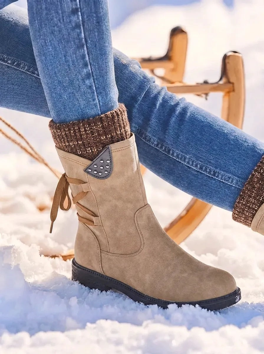 Tan mid-calf winter boot paired with jeans, featuring a brown knitted cuff, side zip and decorative lace-like side detail.