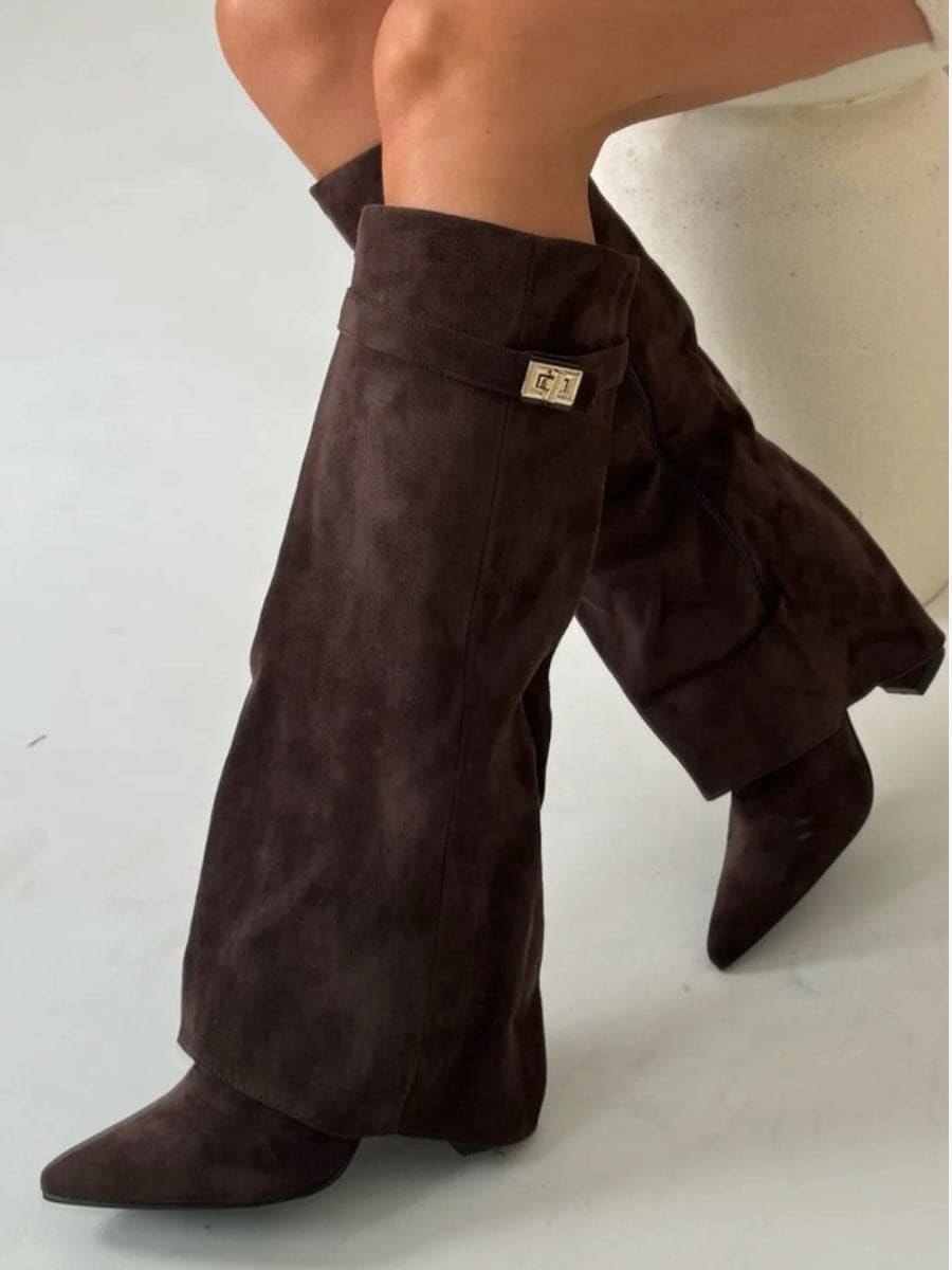 Dark brown knee-high boots crossed at the legs, featuring pointed toes, fold-over cuffs, metallic accents, and low heels.