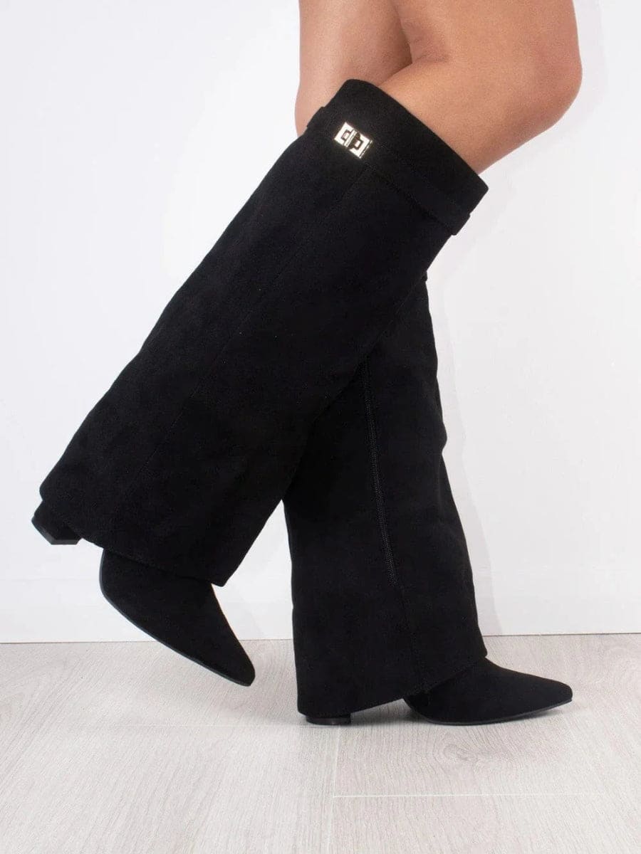 Side view of black knee-high boots with overlapping fold-over shafts, pointed toes, and a small metallic cuff accent.