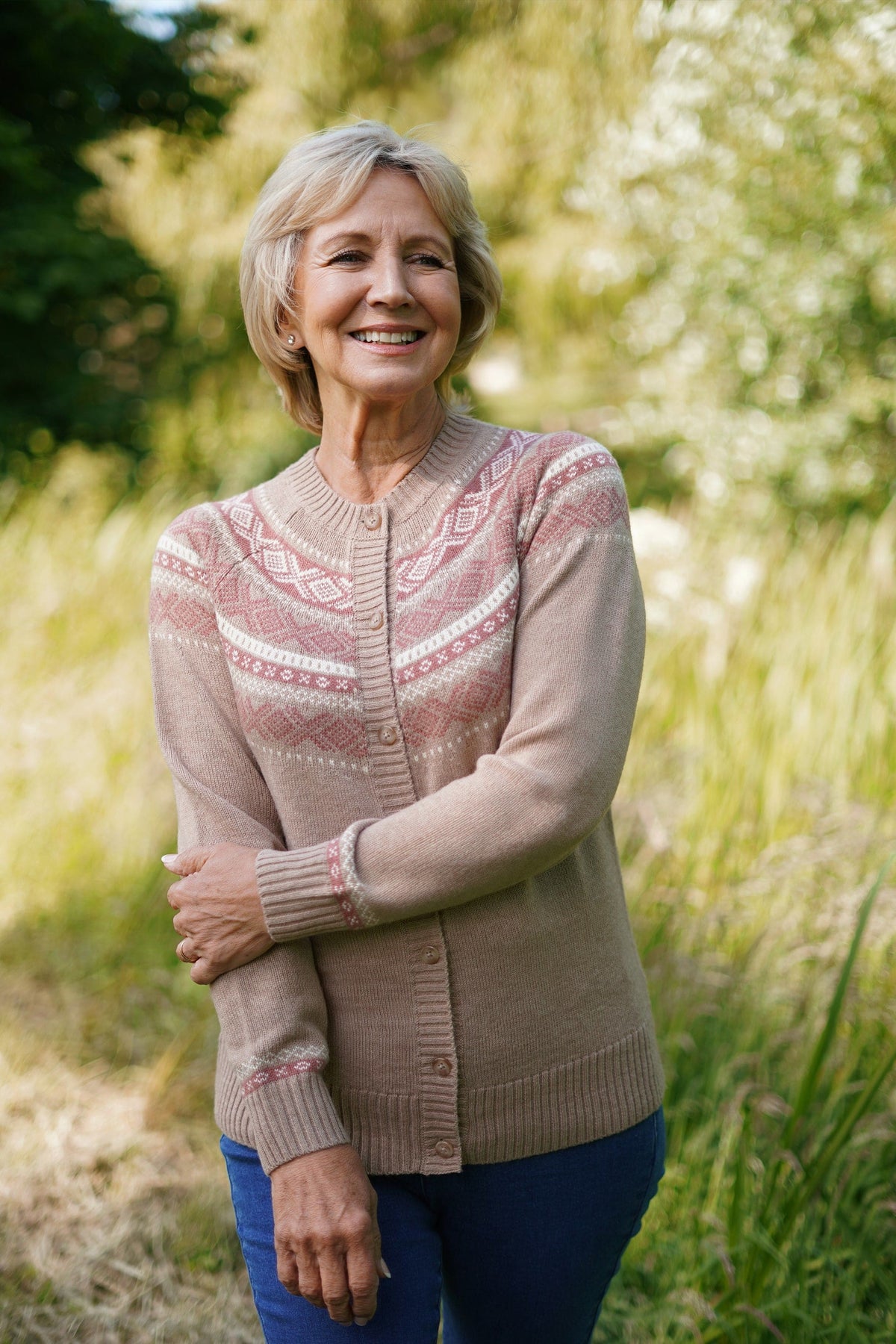 Woman standing outdoors wearing a long-sleeved button-front knit cardigan with a patterned Fair Isle yoke, ribbed crew neck, cuffs and hem, with jeans._0