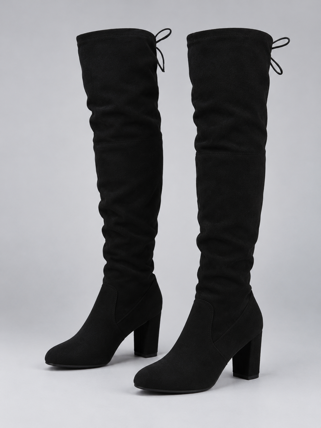 Pair of black over-the-knee boots with gathered shafts, rounded toes, rear tie details, and tall block heels shown from the front and side.