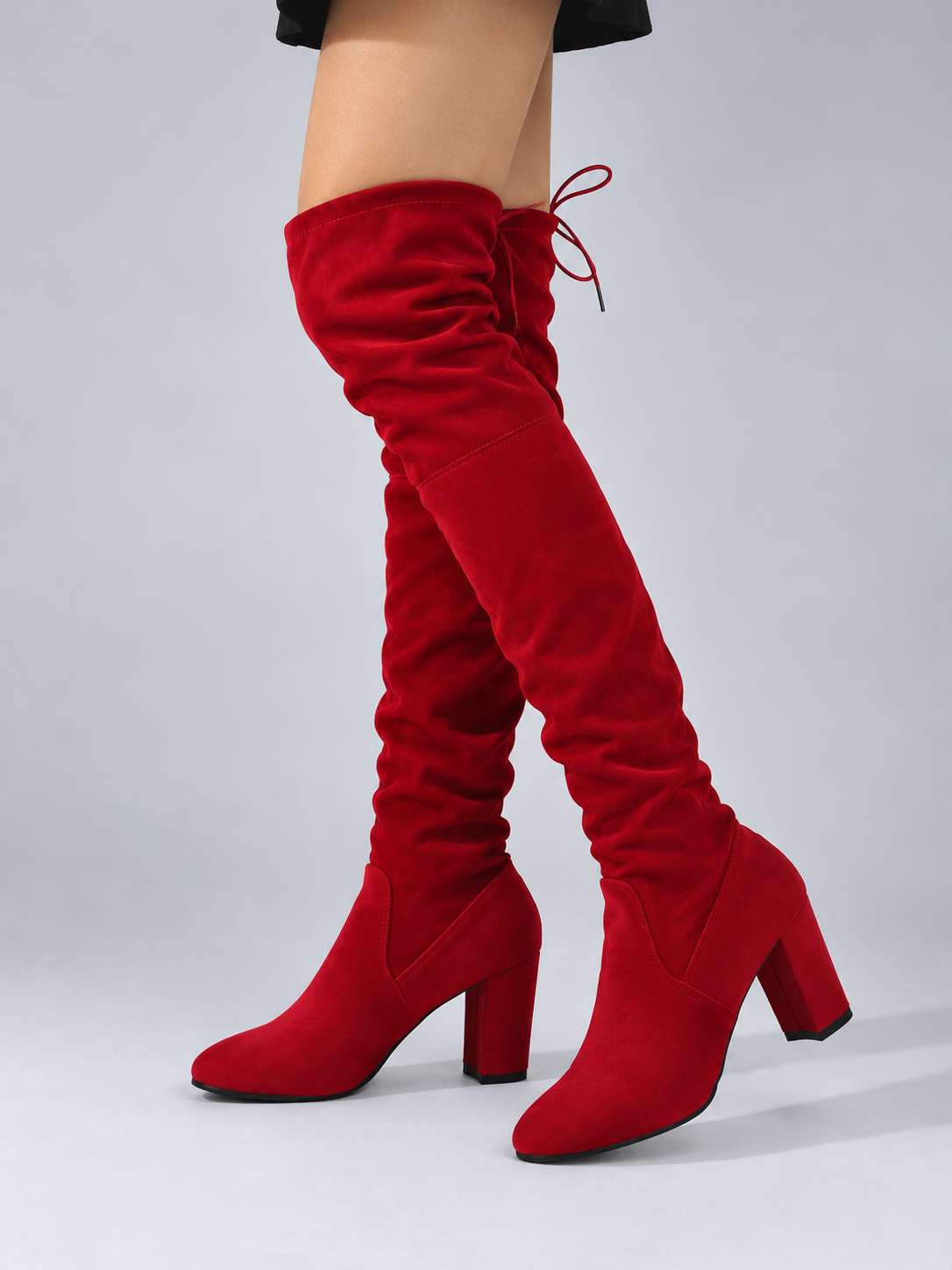 Red over-the-knee boots modeled with crossed legs, showcasing the ruched shafts, rounded toes, rear ties, and raised block heels.