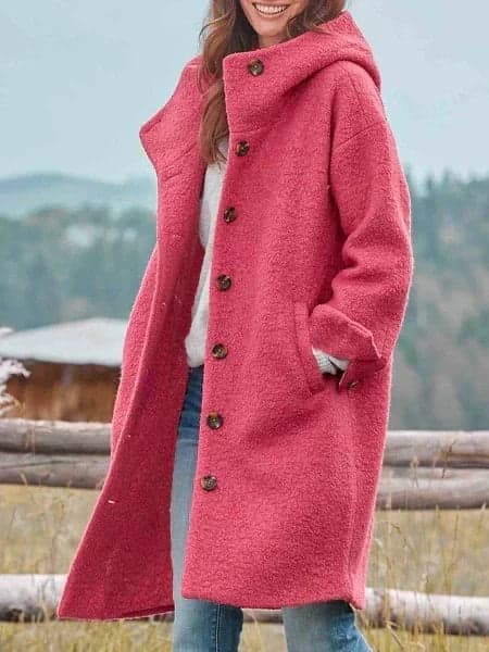 Woman wearing a long hooded coat with a full front button placket, textured surface and two large patch pockets, over a knit jumper and jeans._0
