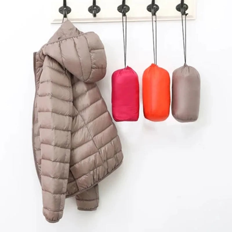 Taupe hooded quilted puffer jacket hanging beside three compact rolled jacket bundles.