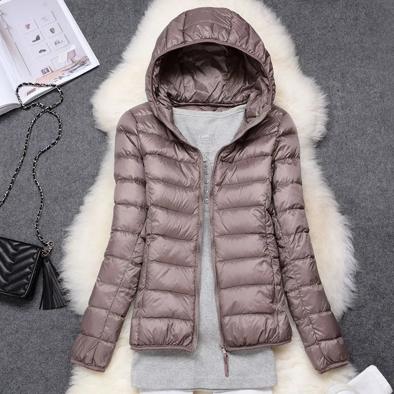 Taupe hooded quilted puffer jacket shown open over a gray outfit on a faux-fur surface.