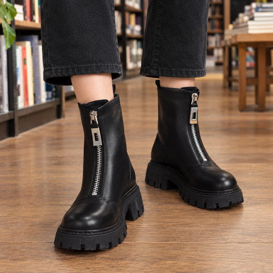 Pair of black ankle boots with prominent front zippers, rounded toes, and chunky lug soles styled with cropped black jeans.