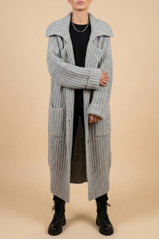 Woman wearing a long open front chunky rib knit cardigan with an oversized fold over collar, two patch pockets and ribbed cuffs, over a top and trousers with lace up boots._0