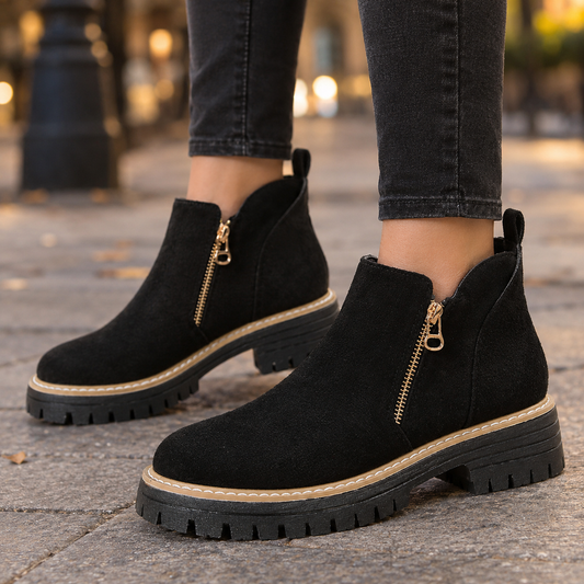 Black ankle boots with gold-tone side zips, rounded toes, low block heels, and chunky lug soles shown with black jeans.