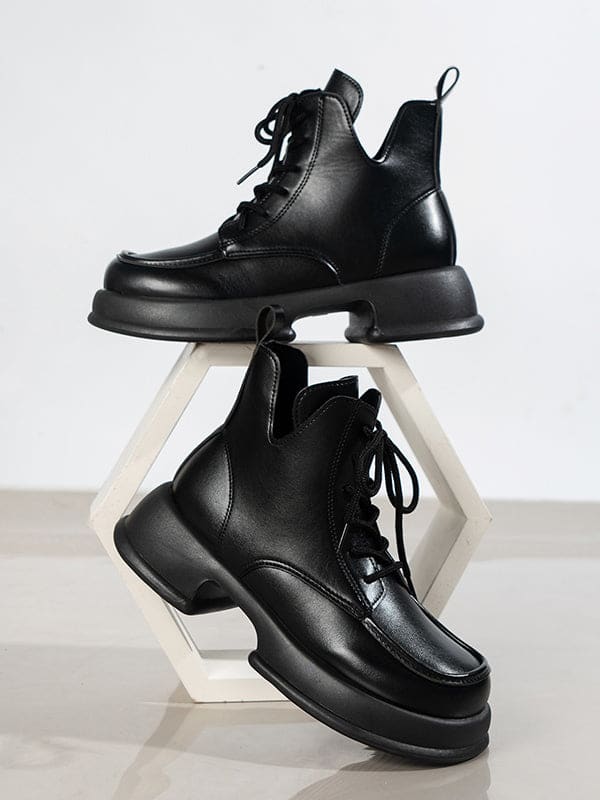 Pair of platform lace-up boots with chunky sole and round toe displayed on a geometric white stand._0