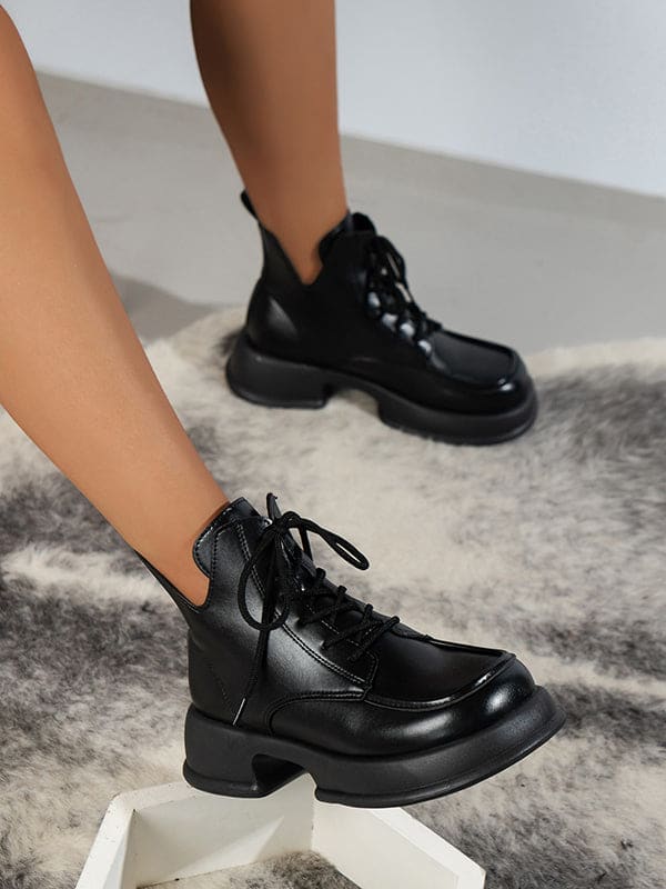 Pair of platform lace-up boots with chunky sole and round toe displayed on a geometric white stand._3
