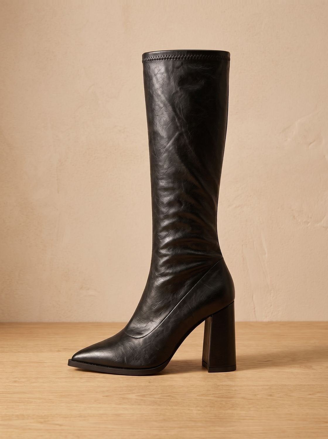 Black pointed-toe knee-high boot shown in profile with a tall shaft and substantial block heel.