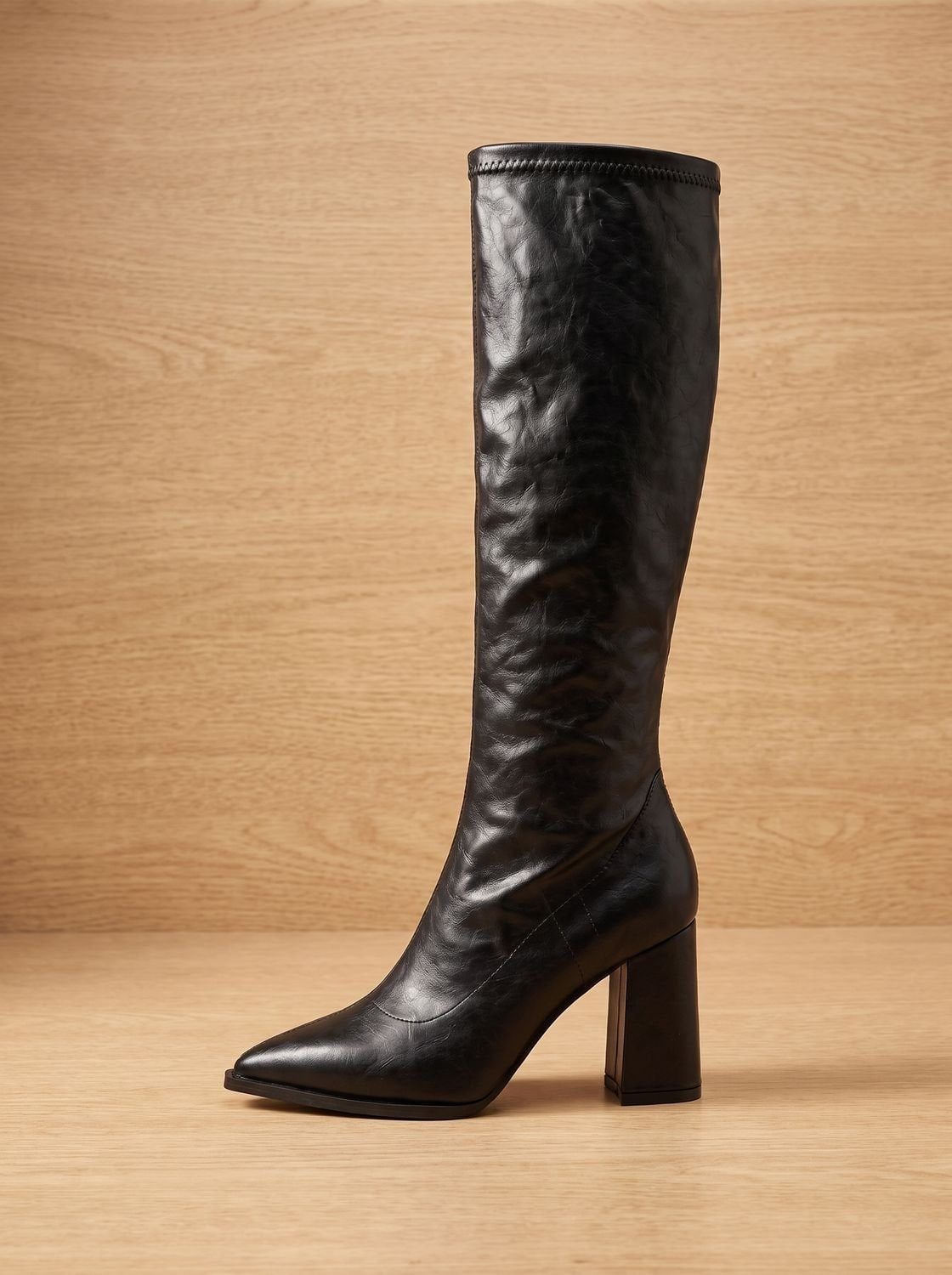 Black knee-high boot angled from the front, highlighting its pointed toe, ruched shaft, and raised block heel.