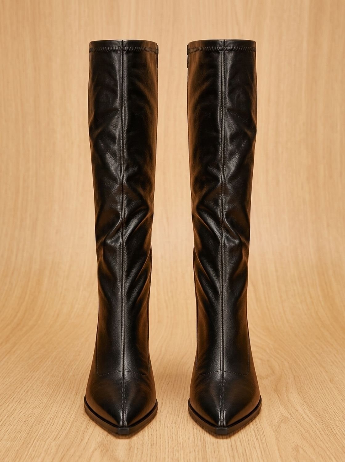 Pair of black pointed-toe knee-high boots viewed from the front, showing their tall matching shafts and block heels.