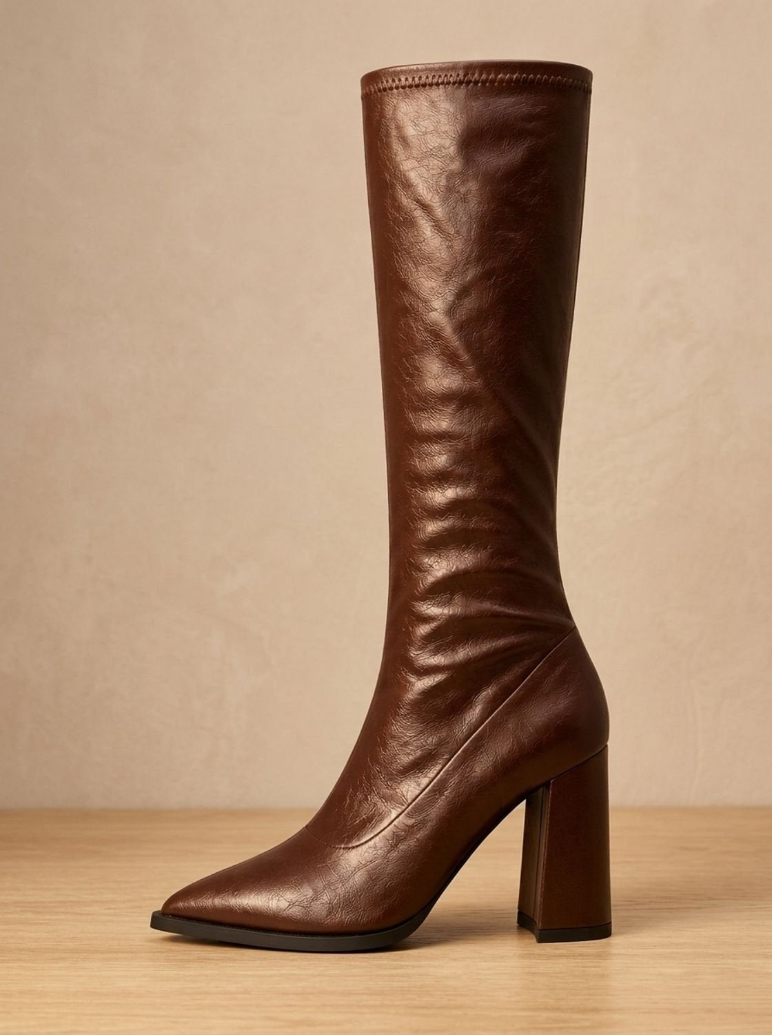 Brown pointed-toe knee-high boot in side profile with a tall ruched shaft and block heel.