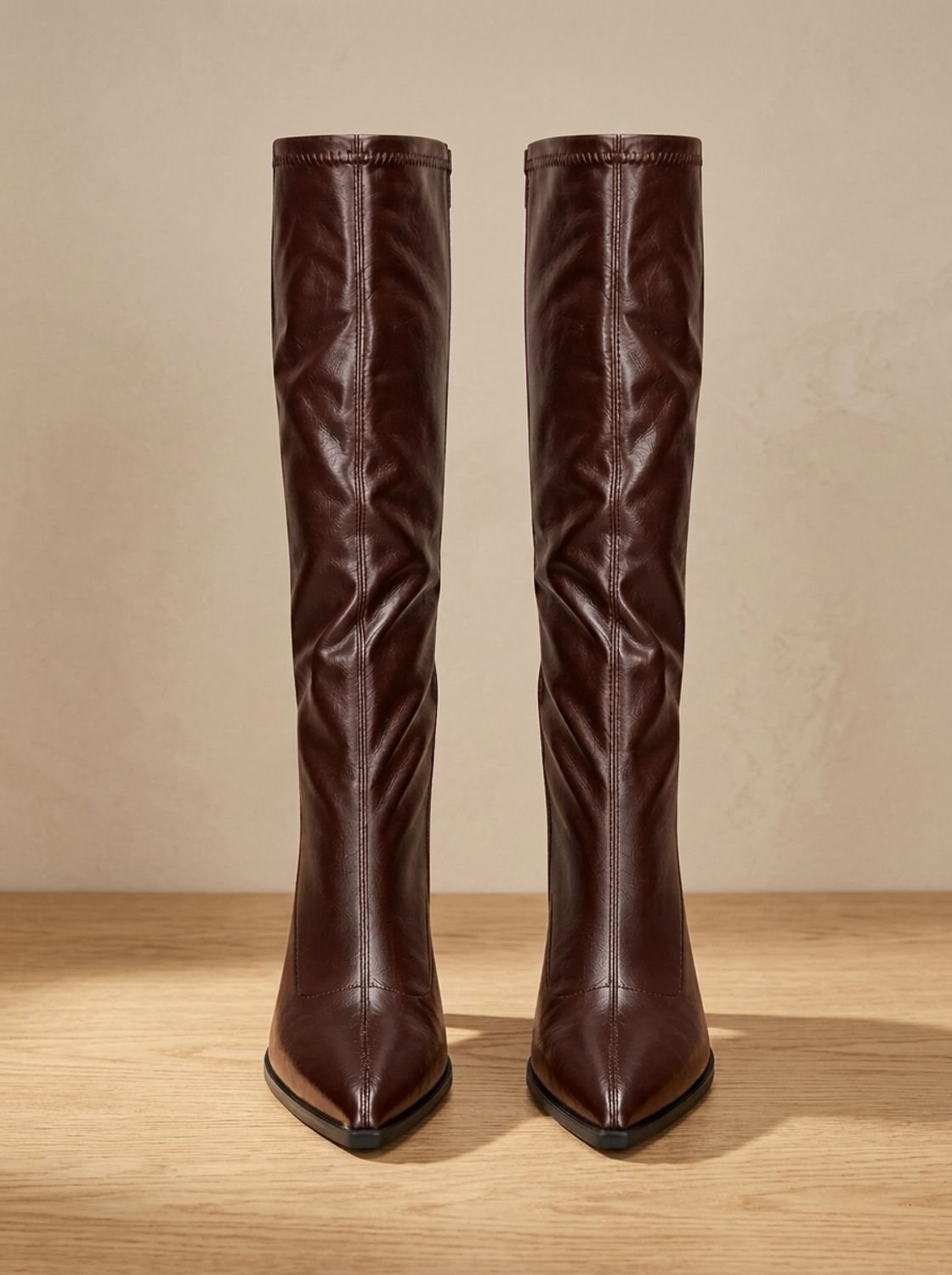 Pair of brown pointed-toe knee-high boots facing forward, with stitched tall shafts and matching block heels.