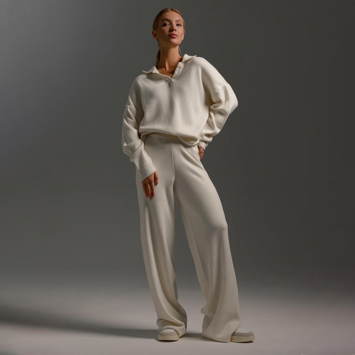 Model wearing the white polo sweater and wide-leg pants with one hand resting at the hip.