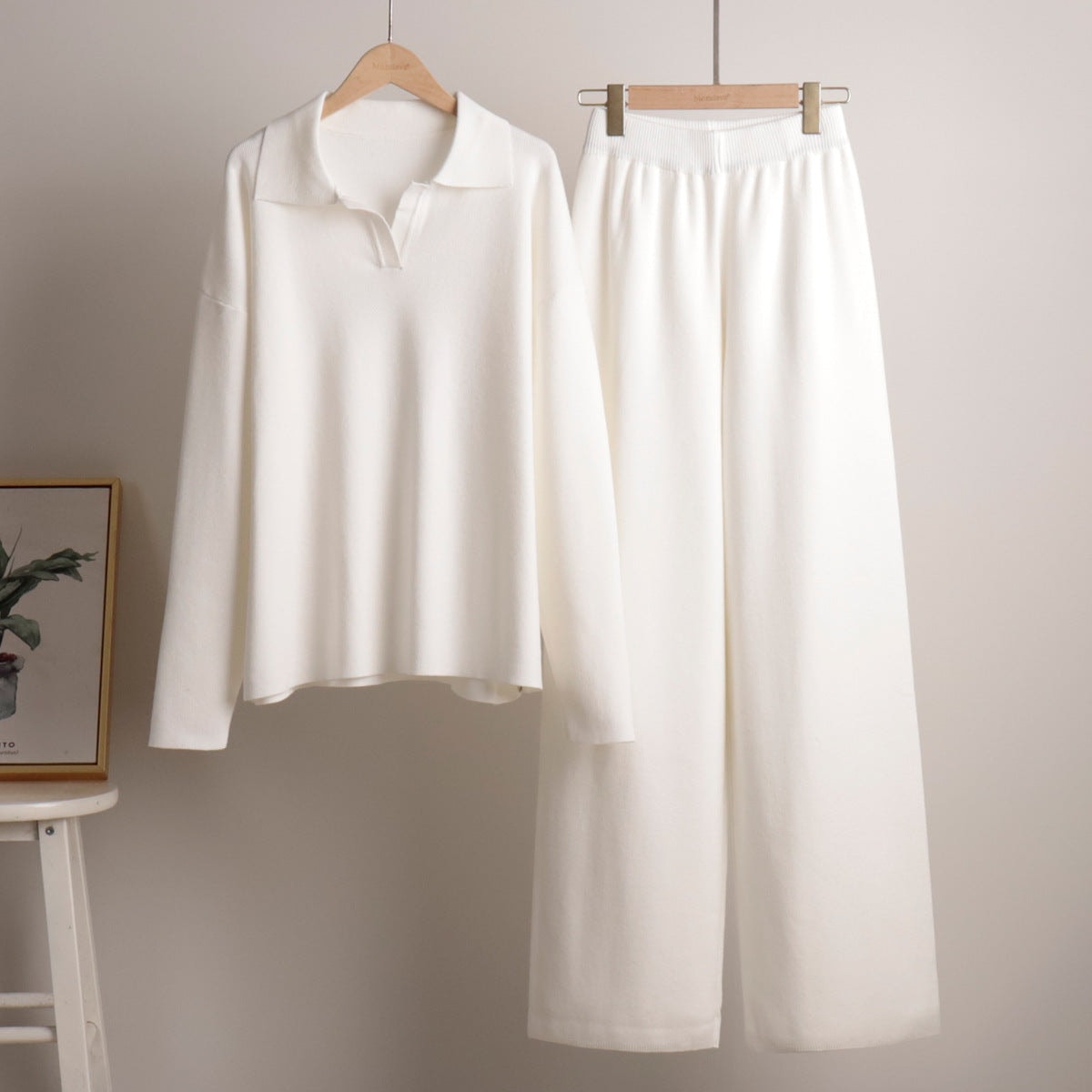 White polo sweater and wide-leg pants displayed separately on wooden hangers.