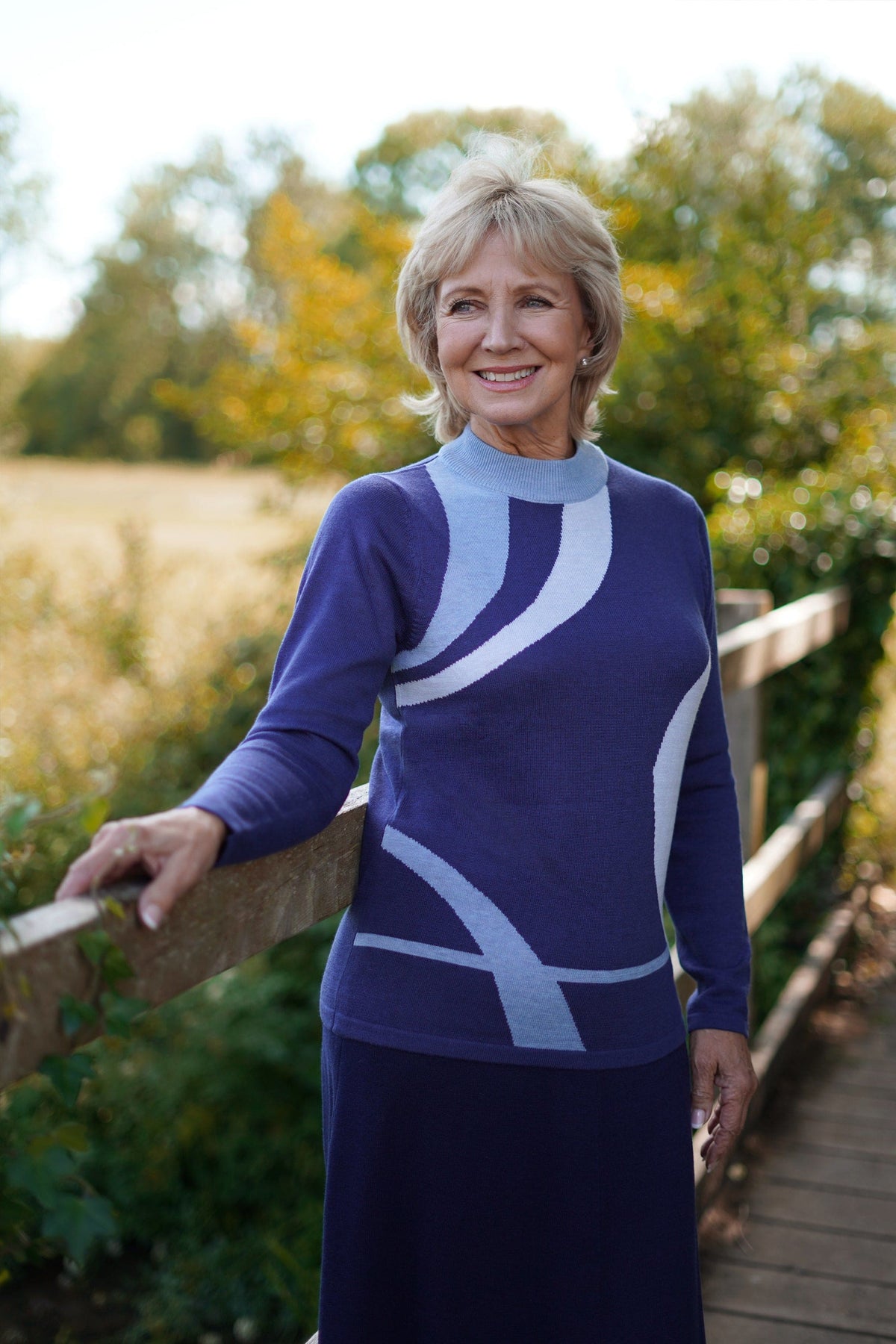 Woman wearing a long sleeve mock neck knit jumper with curved contrast panels across the front, worn with a long knit skirt outdoors._0