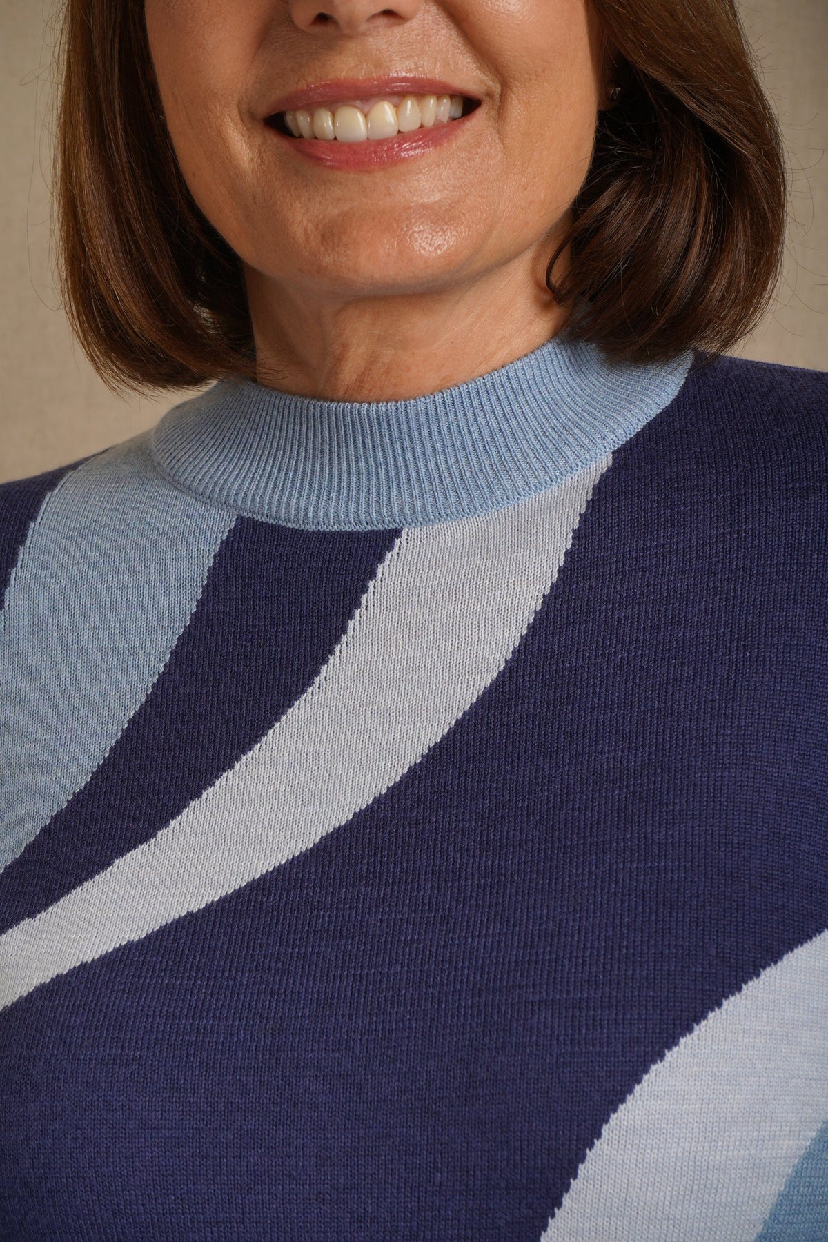 Woman wearing a long sleeve mock neck knit jumper with curved contrast panels across the front, worn with a long knit skirt outdoors._5