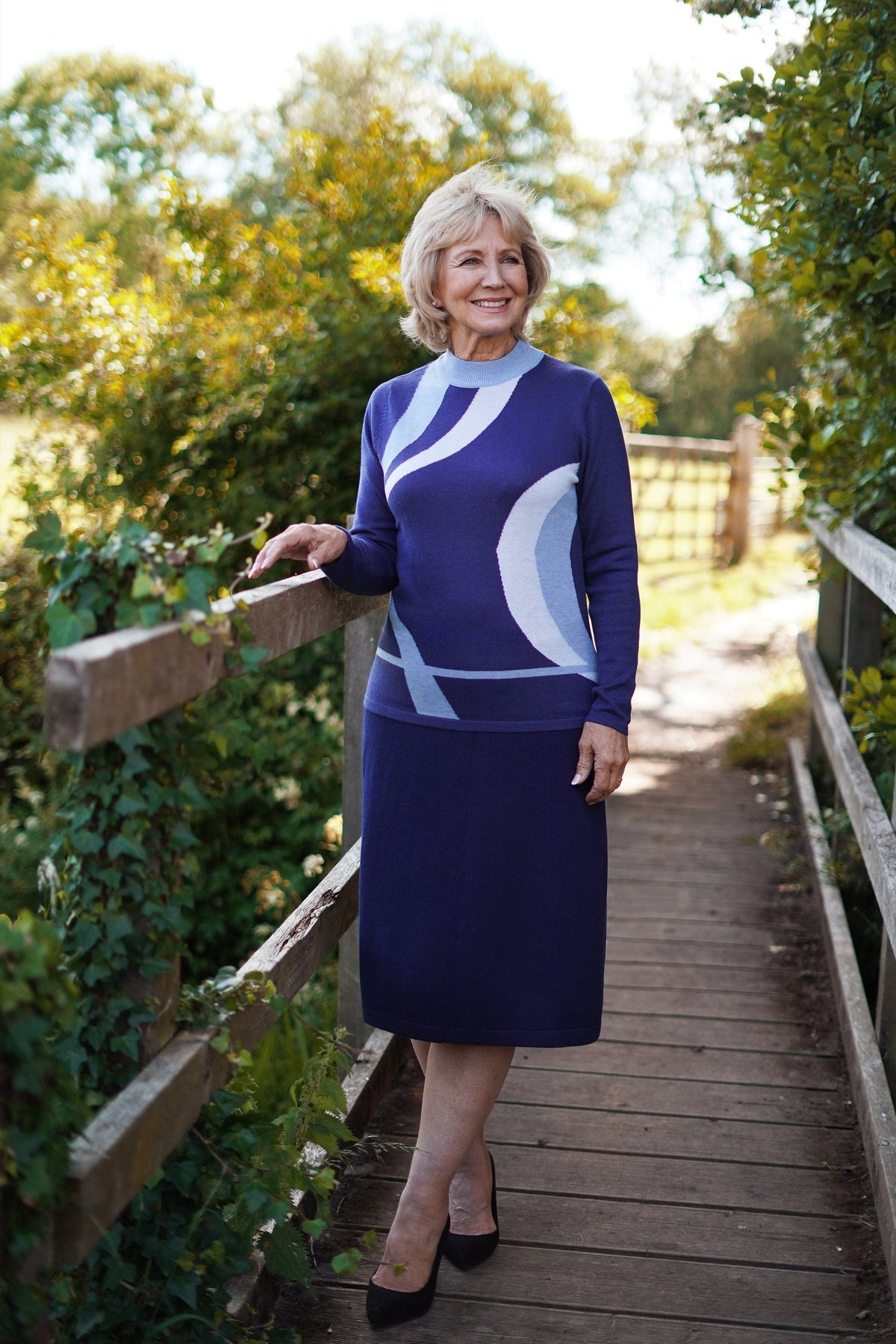 Woman wearing a long sleeve mock neck knit jumper with curved contrast panels across the front, worn with a long knit skirt outdoors._6