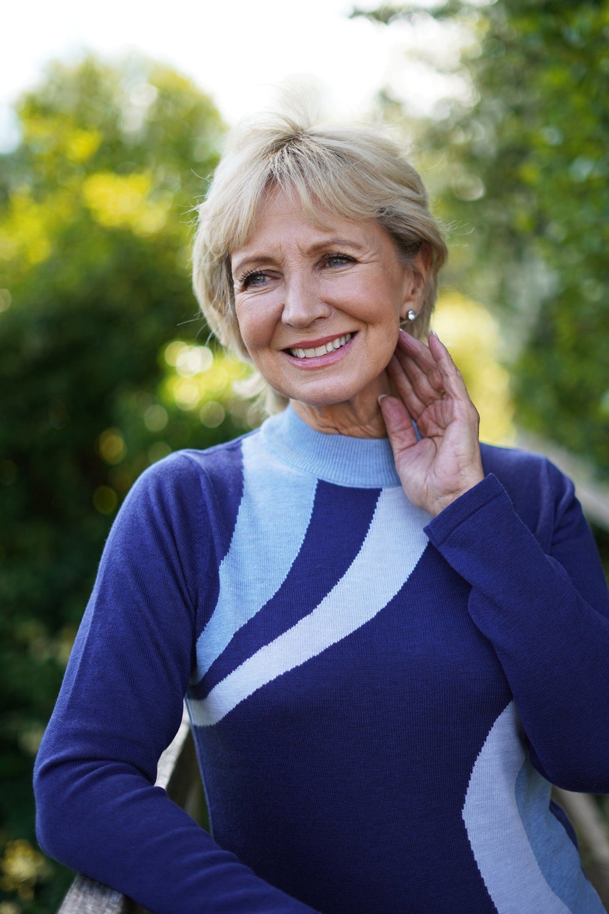 Woman wearing a long sleeve mock neck knit jumper with curved contrast panels across the front, worn with a long knit skirt outdoors._7