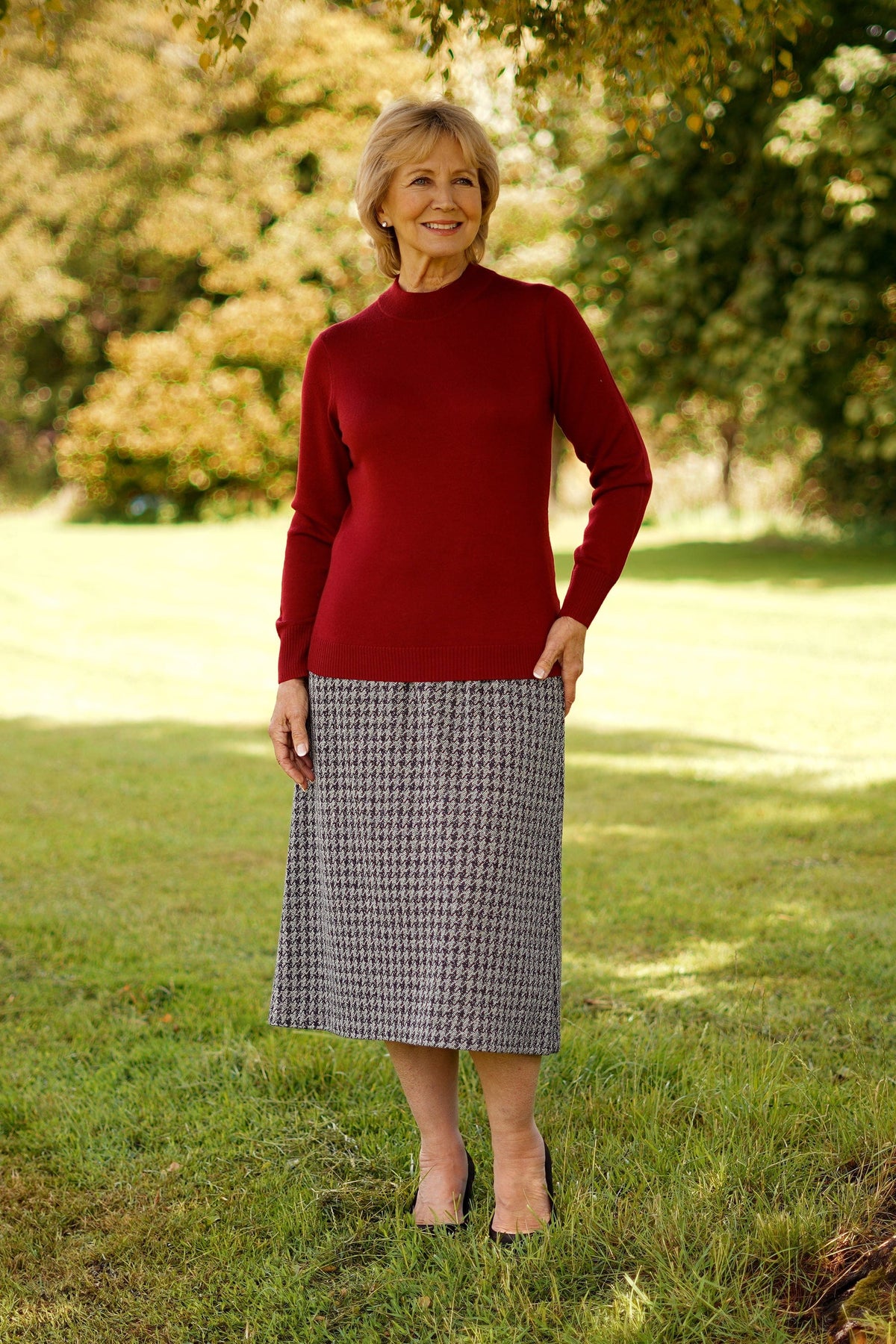 Woman standing outdoors wearing a long sleeve mock neck knitted jumper with ribbed cuffs and hem, paired with a houndstooth midi skirt._18