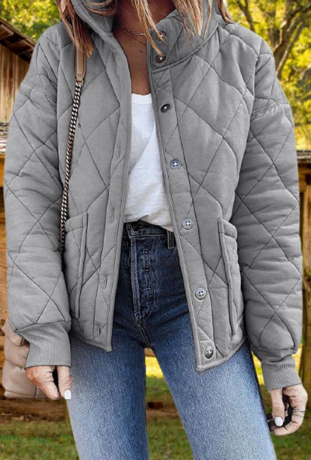 Woman wearing a diamond quilted button front jacket with stand collar, ribbed cuffs and two front pockets, over a white tee and jeans._0