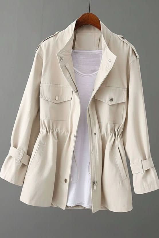 Utility style jacket with stand collar, zip and snap front, two flap chest pockets, two hip pockets, drawstring waist and tabbed cuffs, shown on a wooden hanger over a white top._7
