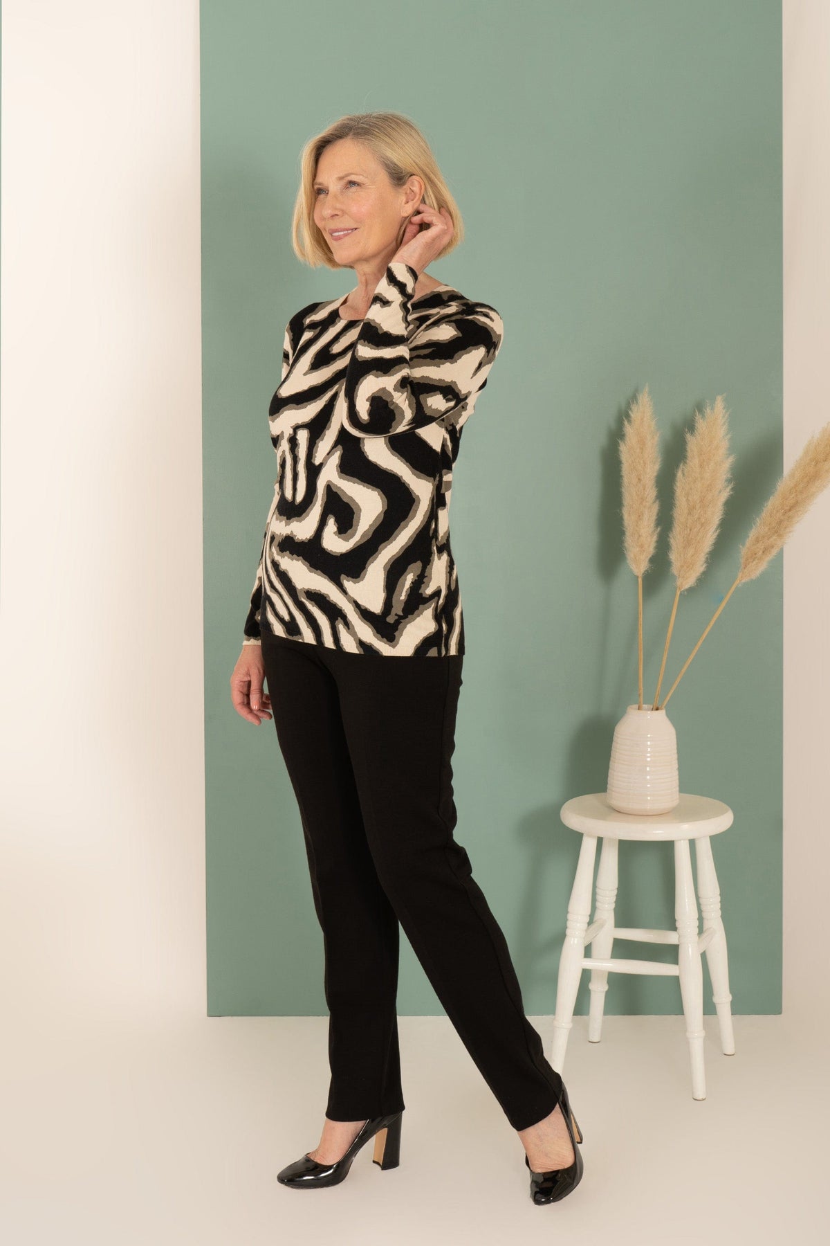 Woman wearing a long sleeve round neck knit jumper with a bold swirling animal print, styled with dark trousers._1